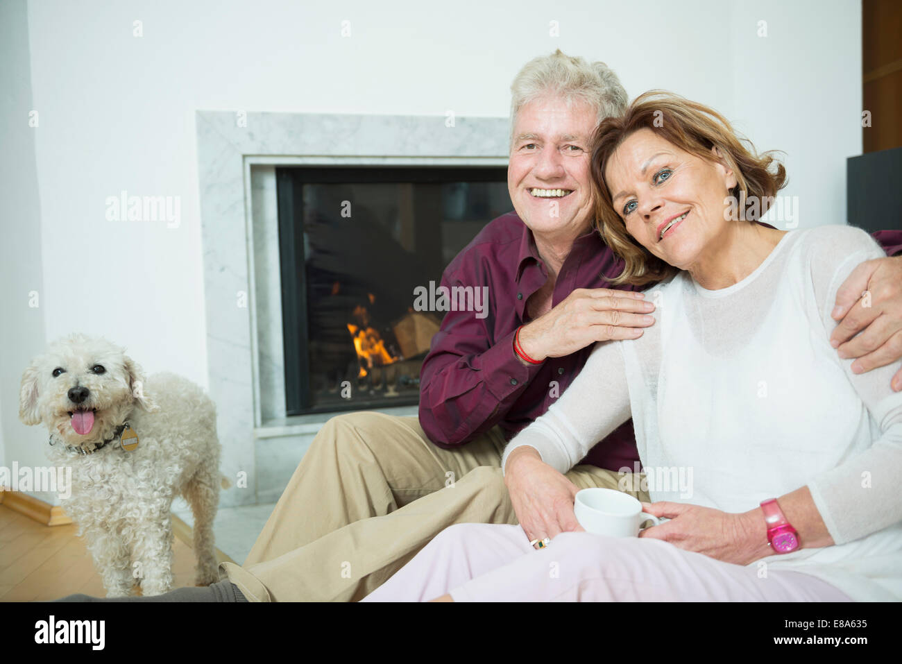 Portrait of senior couple with dog sitting in front of fireplace ...