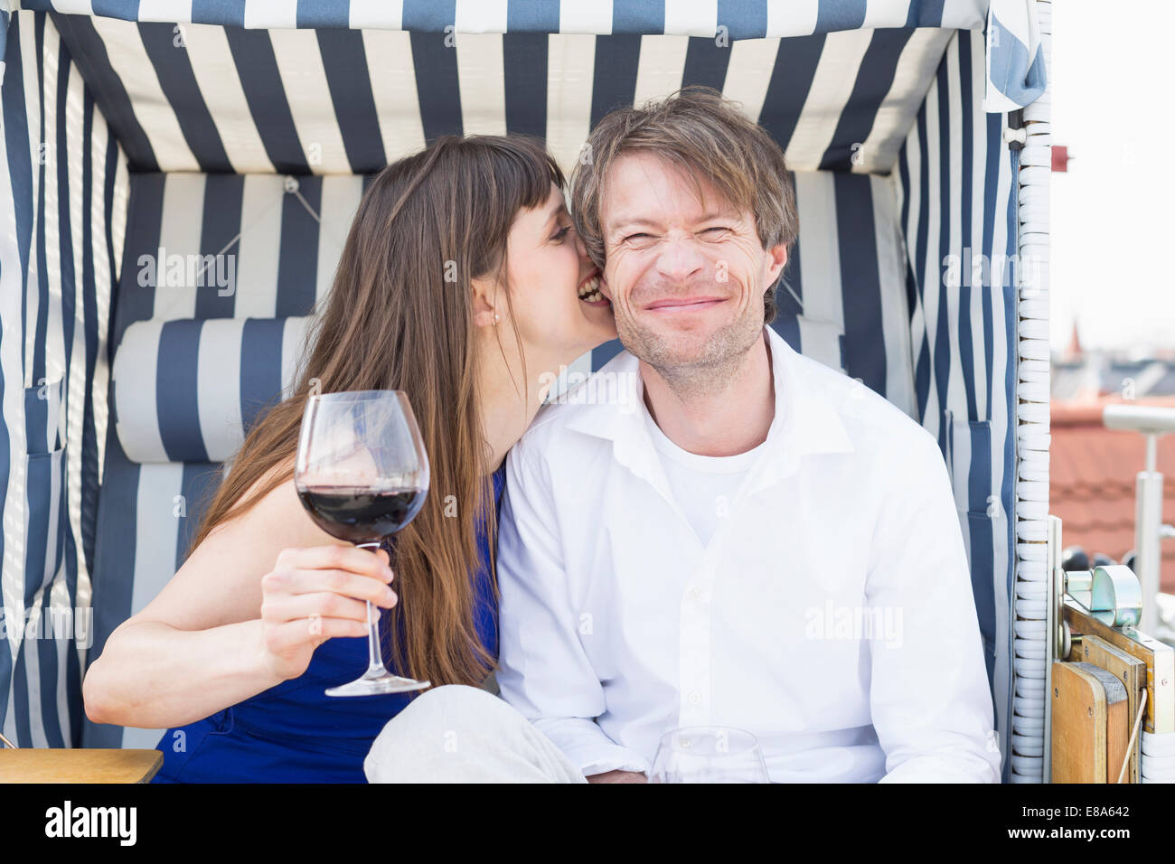 Couple having vine in roofed wicker beach chair, smiling Stock Photo