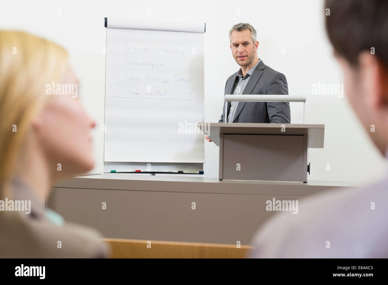 Businesspeople At Speakers Desk In Auditorium With Flip Chart