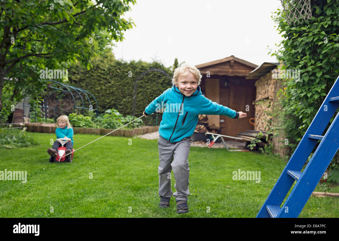 Older brother pulling sister on toy car in garden Stock Photo