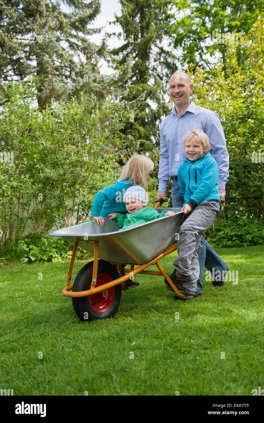 Father in garden pushing kids in wheelbarrow Stock Photo
