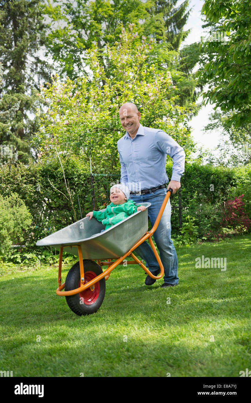 Father pushing baby son in wheelbarrow garden Stock Photo