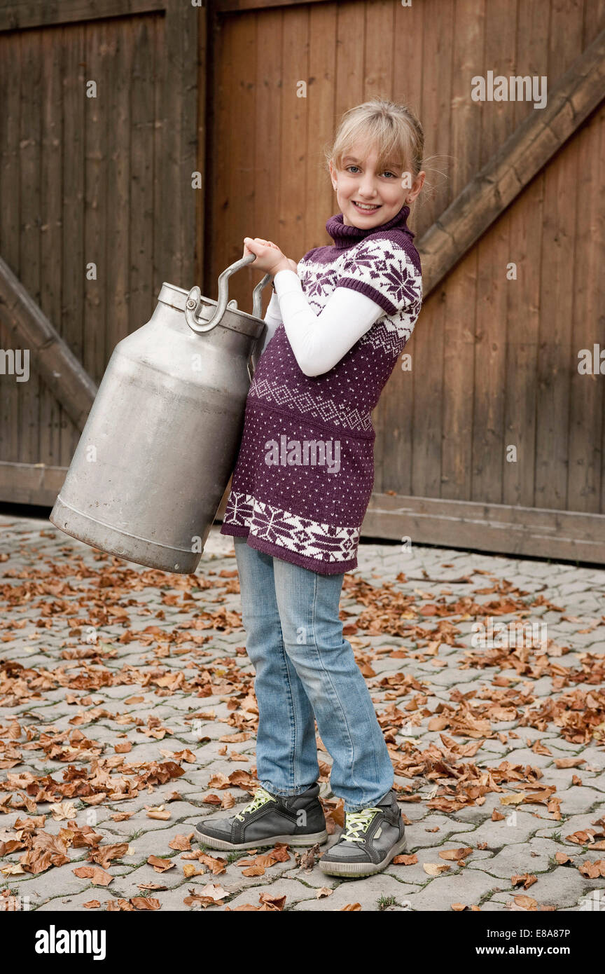 Smiling girl carrying milk churn on farm Stock Photo