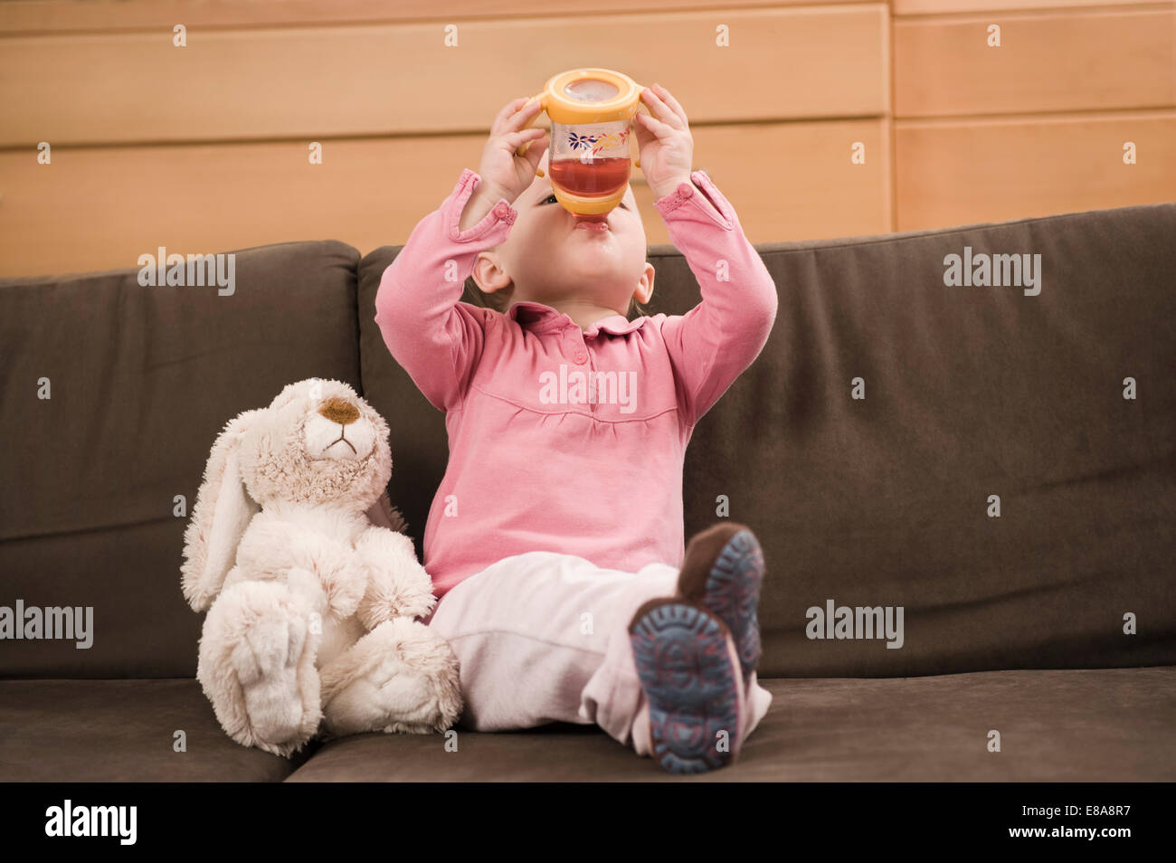 Baby girl 18 months sitting on sofa drinking juice Stock Photo Alamy