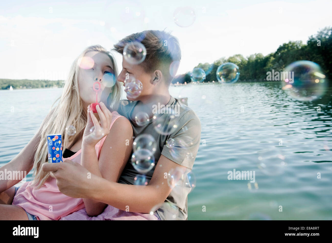 Teenage couple blowing soap bubbles on a jetty at lake Stock Photo
