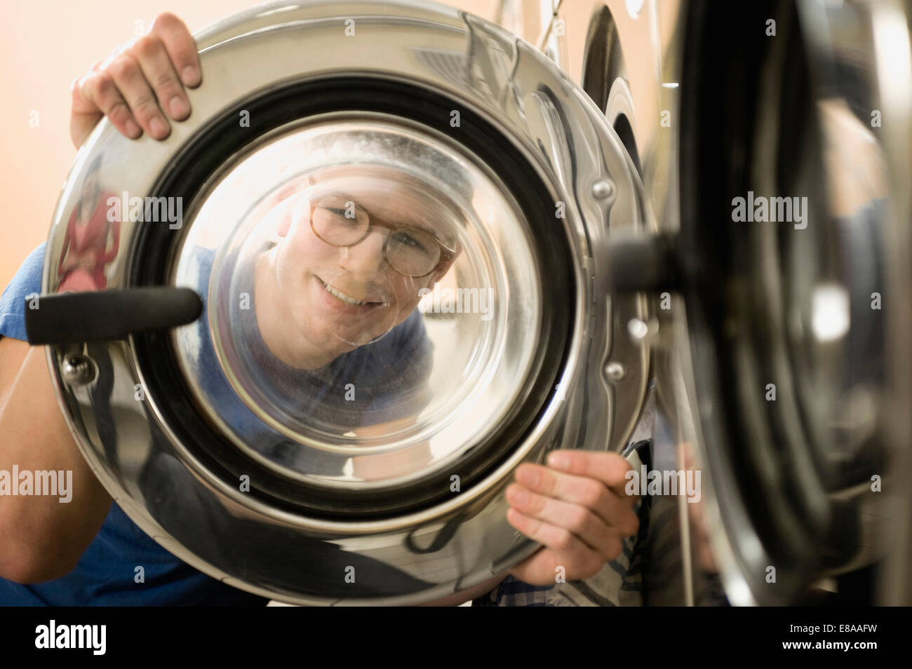 Young man looking through window of washing machine, smiling Stock Photo