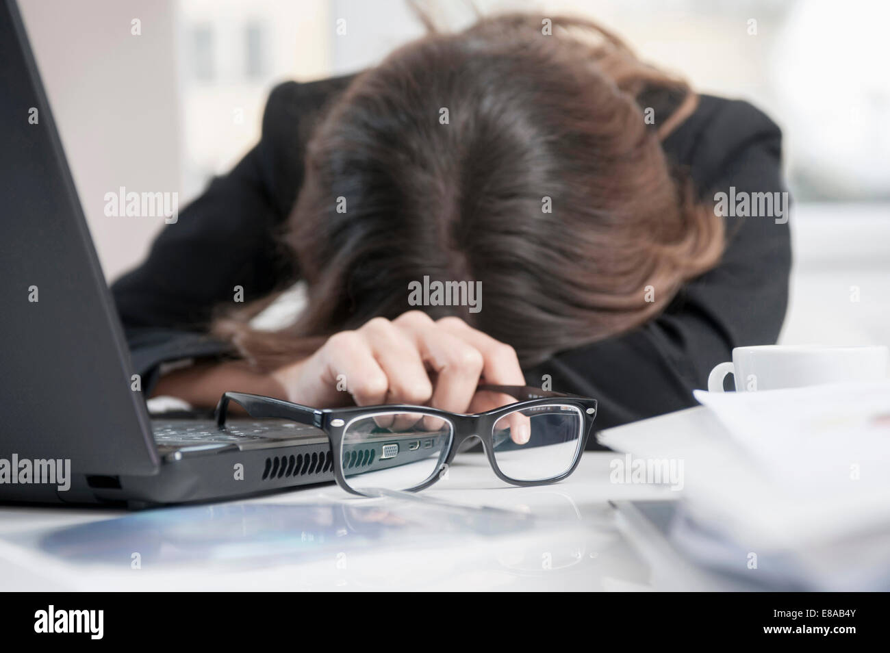 Young overburdened businesswoman with head on desk at her workplace