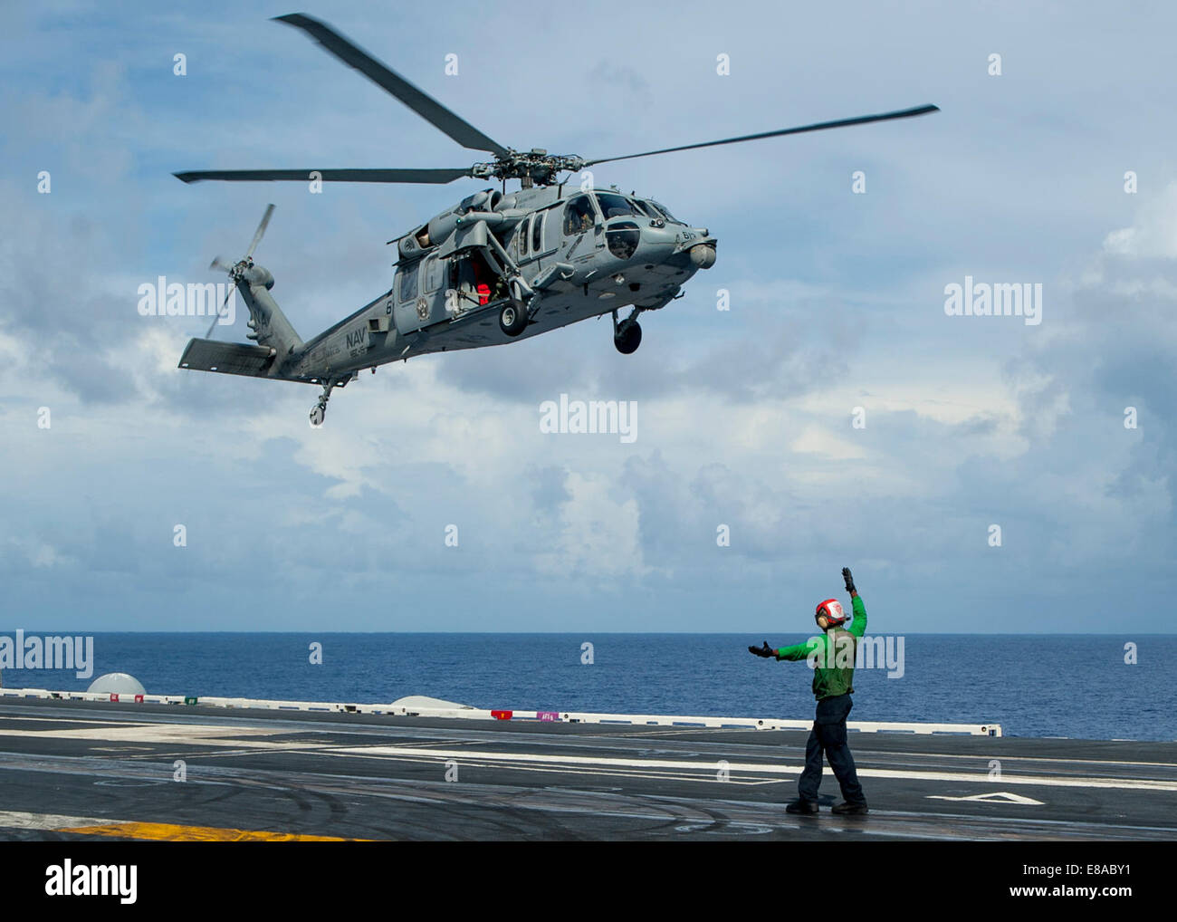 U.S. Navy Aviation Machinist?s Mate 3rd Class Alex Lasan signals the pilots of an MH-60S Seahawk helicopter assigned to Helicopter Sea Combat Squadron (HSC) 15 to land on the flight deck of the aircraft carrier USS Carl Vinson (CVN 70) Sept. 22, 2014, in Stock Photo