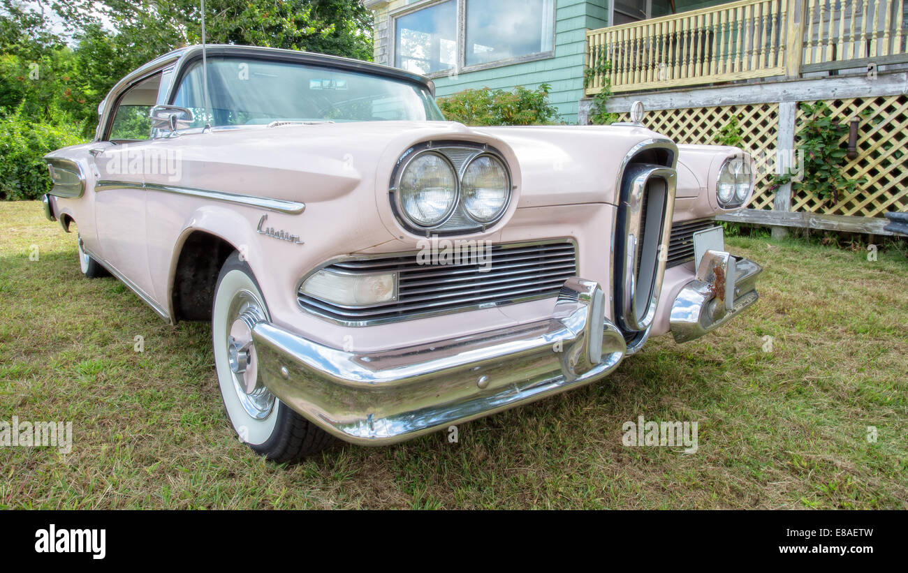 A classic pink Ford Edsel from the 50s in front of an old rundown house. Stock Photo