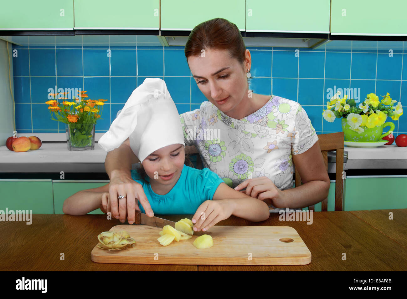 Mother teaches daughter to cut the potatoes in the kitchen Stock Photo