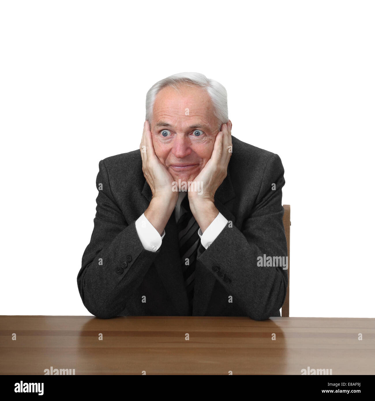Astonished senior man sits at table isolated on white background Stock Photo