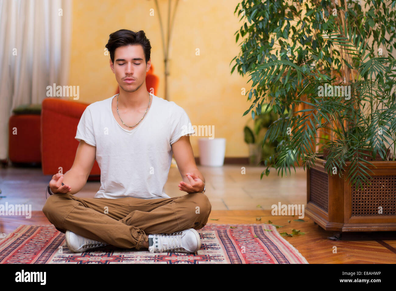 Young man meditating on his living room floor sitting in the lotus ...