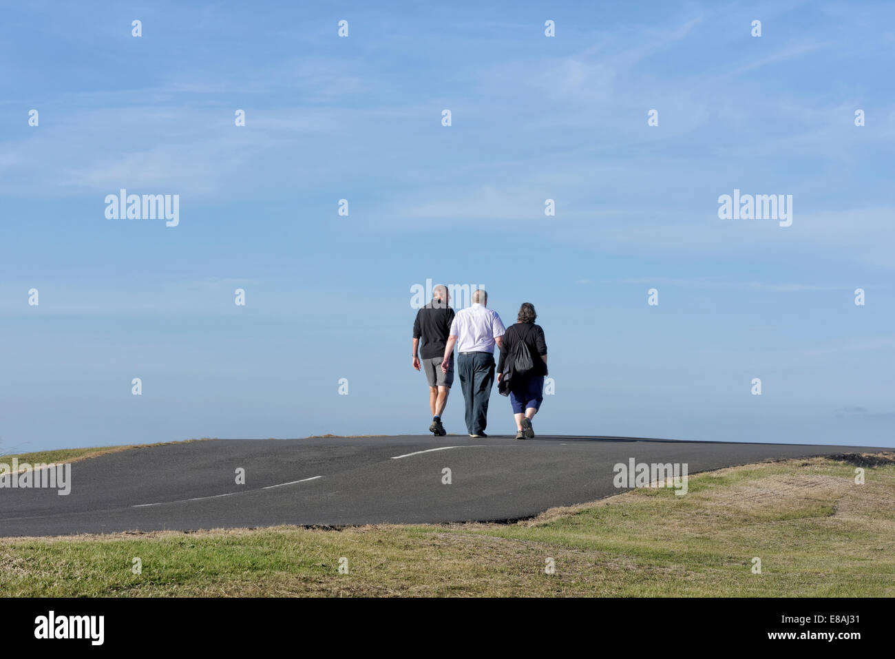 Three people (2 men and a woman) walk away from the camera along a coastal path in Blackpool, Lancashire, UK Stock Photo