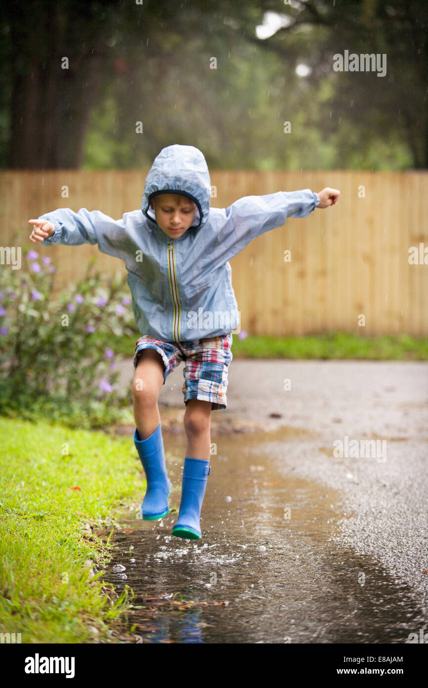 Boy in rubber boots jumping in rain puddle Stock Photo Alamy
