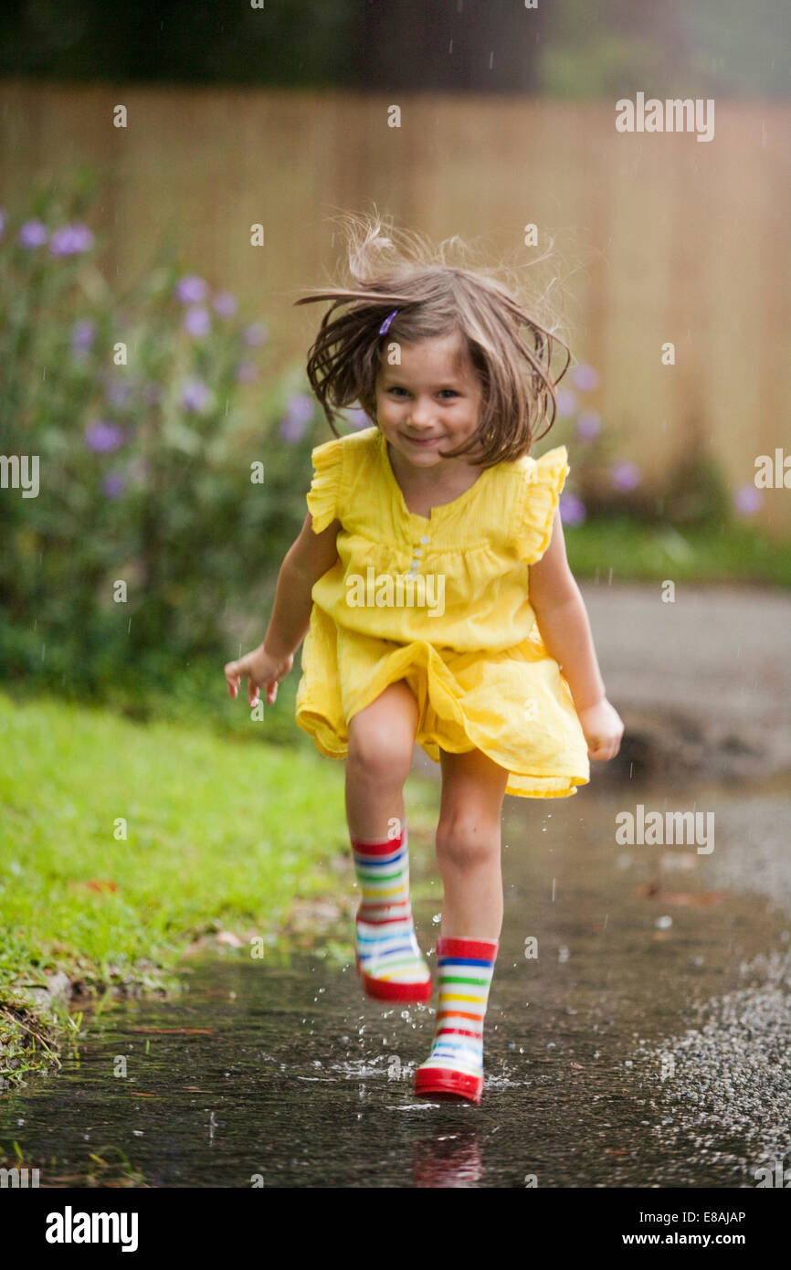 Girl wearing rubber boots running in rain puddle Stock Photo - Alamy