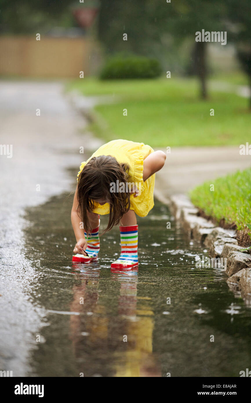 Girl wearing rubber boots picking leaf from rain puddle Stock Photo - Alamy