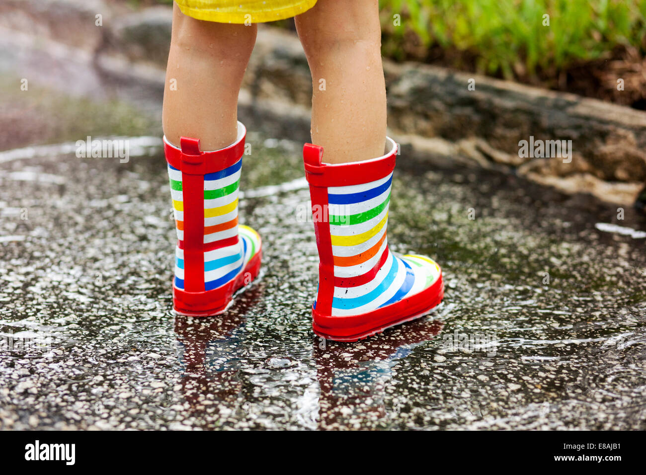 Legs of girl wearing rubber boots standing in rain puddle Stock Photo