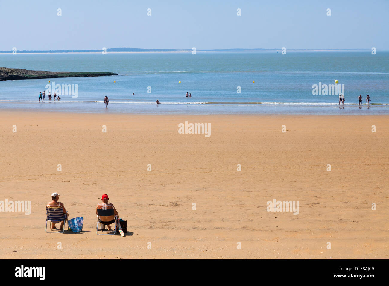 Middle aged couple sitting on folding chairs in the sunshine on fairly quiet beach. Stock Photo