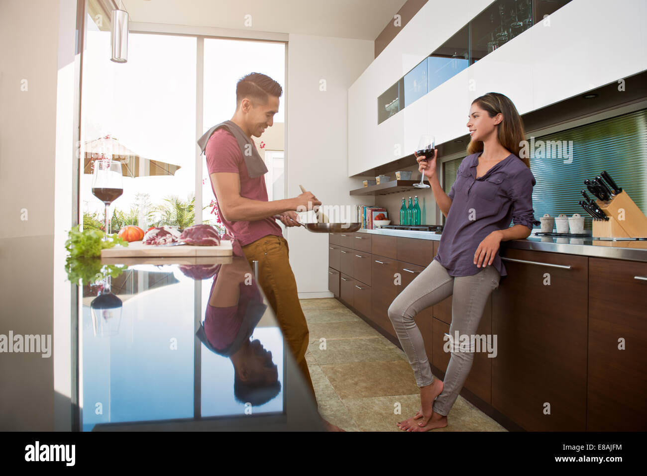 Couple chatting and drinking wine whilst cooking in kitchen Stock Photo