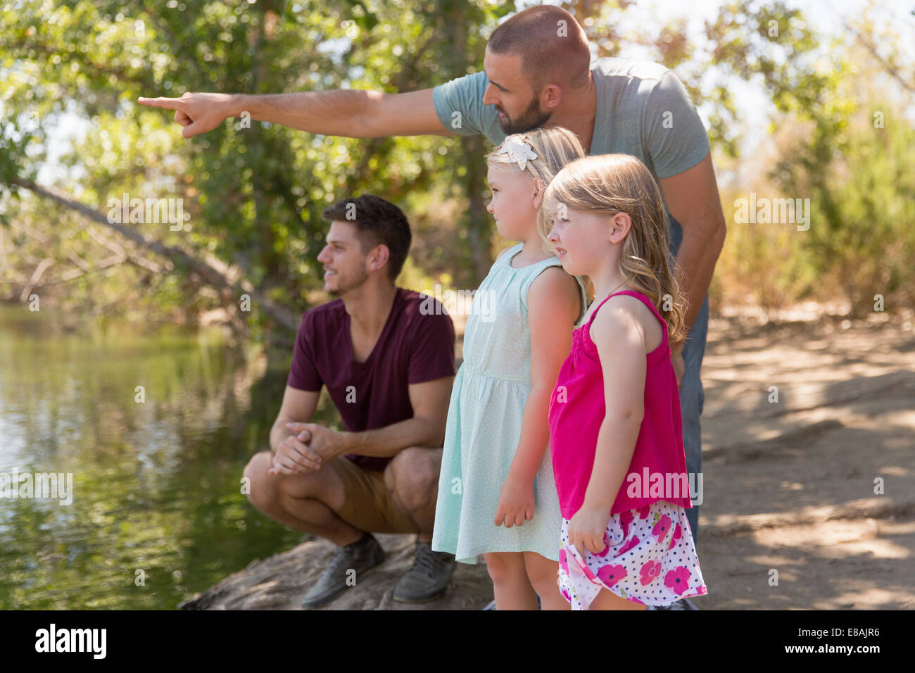 Male couple looking from riverbank with two daughters Stock Photo