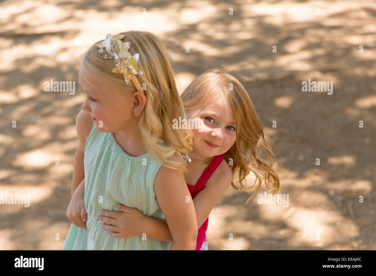 Young girl hiding behind sister in park Stock Photo