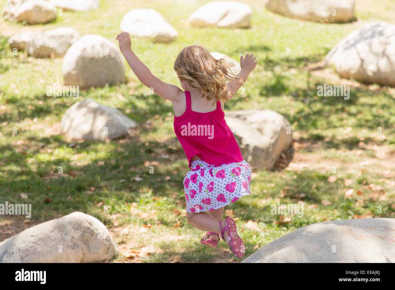 Young girl jumping from boulders in park Stock Photo