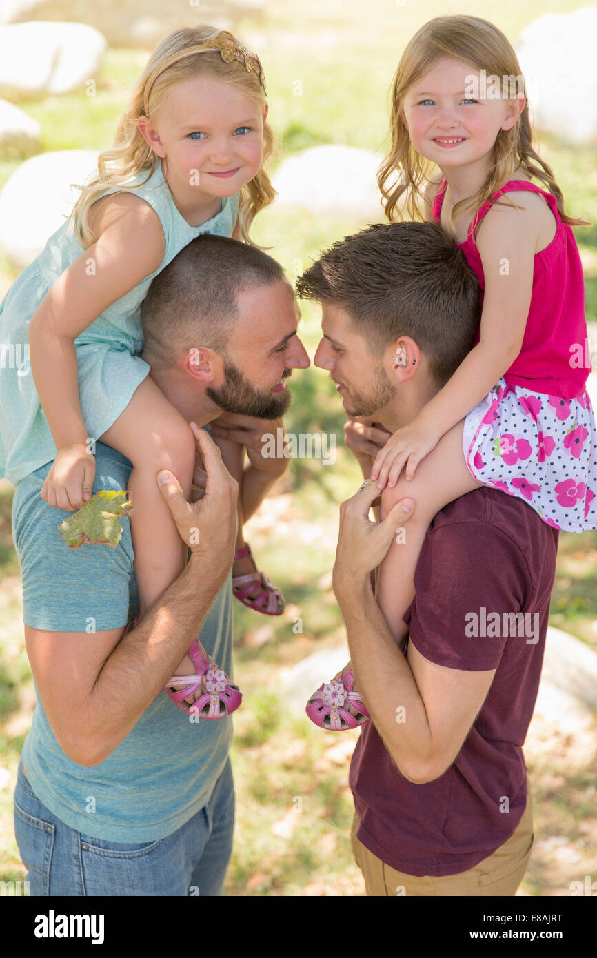 Two sisters sitting on both fathers shoulders in park Stock Photo