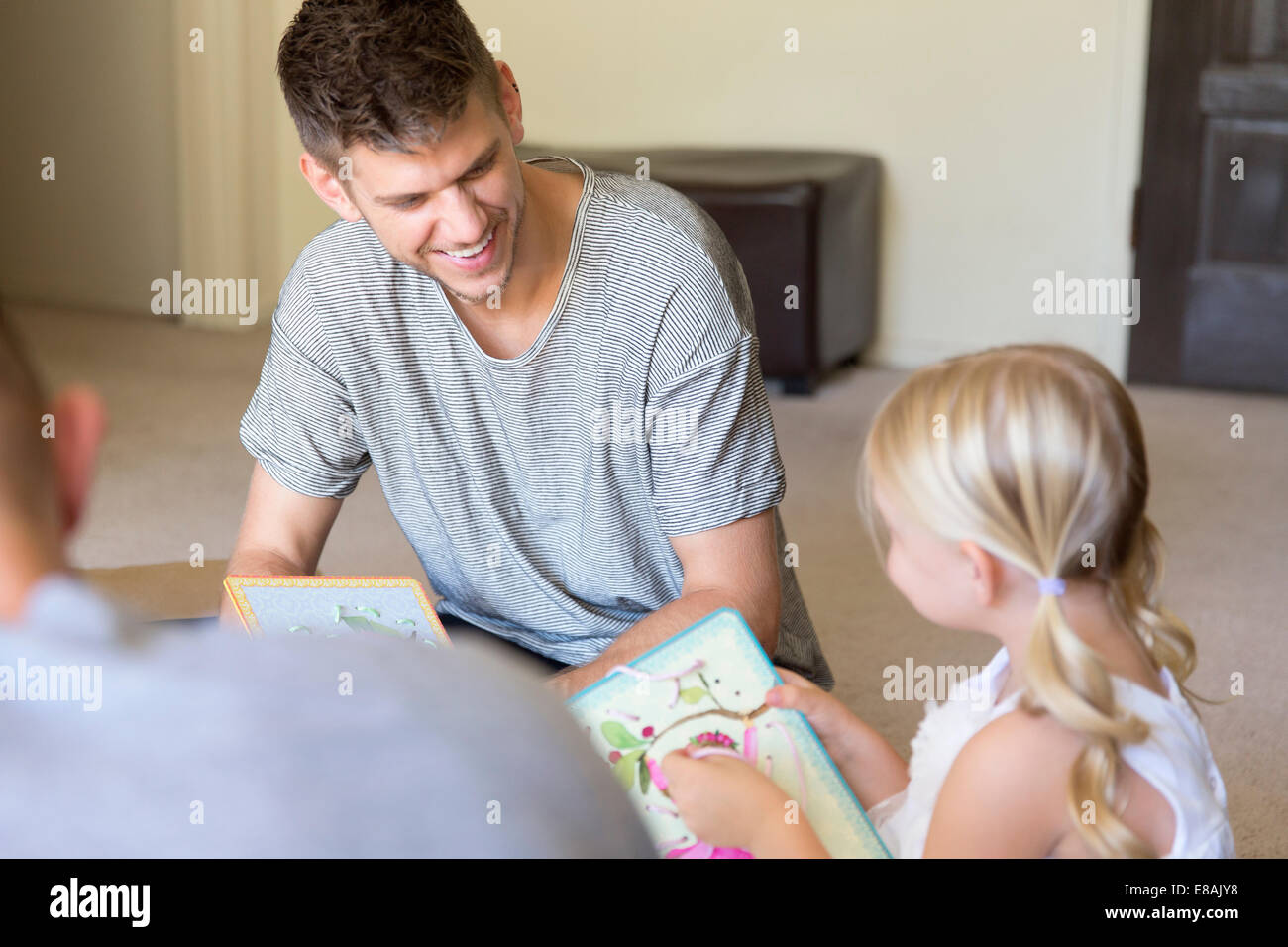 Male couple and daughter threading picture books in sitting room Stock Photo
