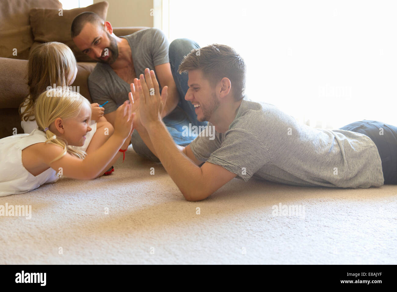 Male couple and two daughters playing clapping game on sitting room floor Stock Photo