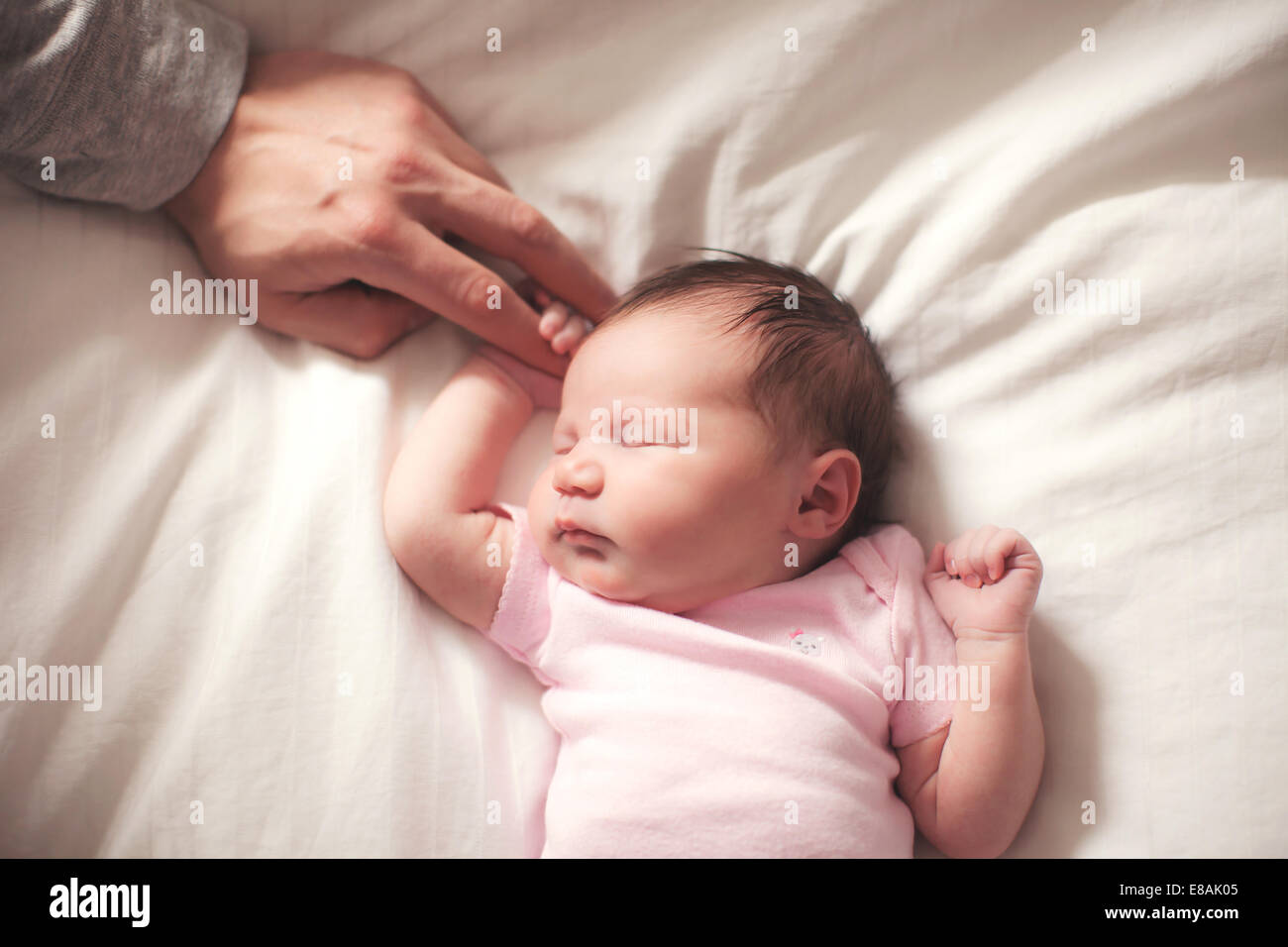 Baby girl sleeping, hands held by father Stock Photo