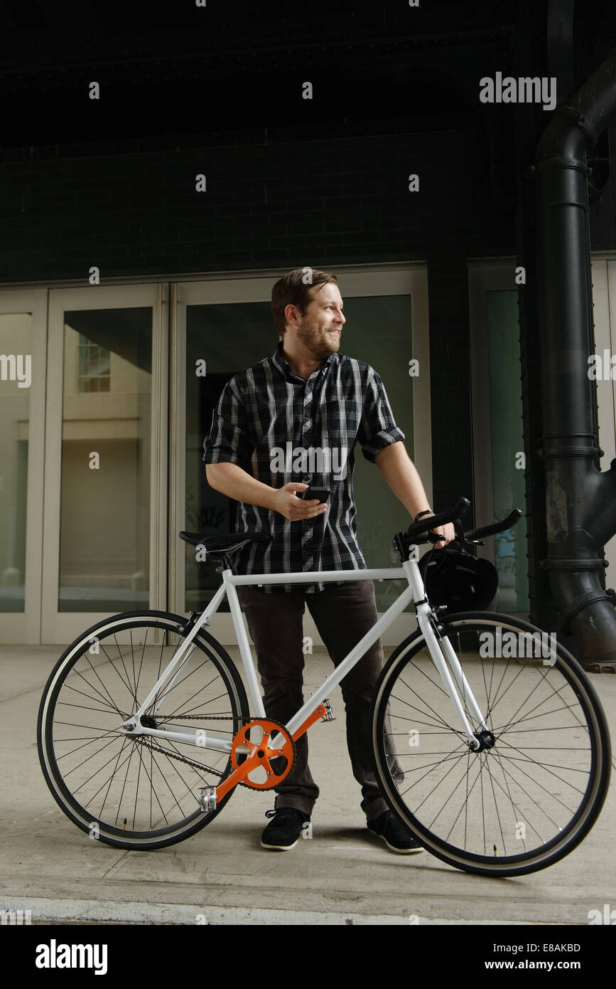Male cycle messenger checking directions on smartphone outside office Stock Photo
