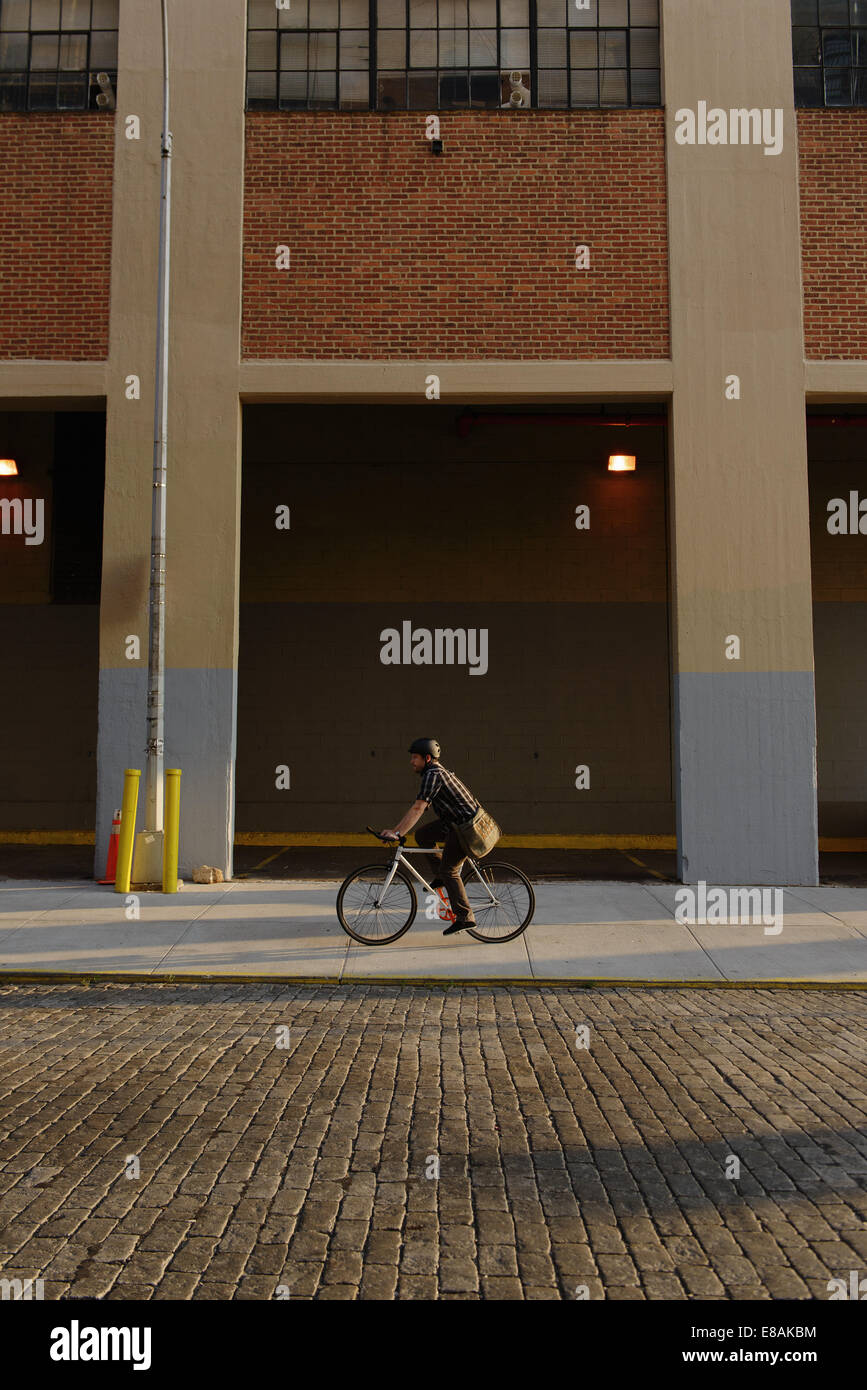 Male messenger cycling along city sidewalk Stock Photo