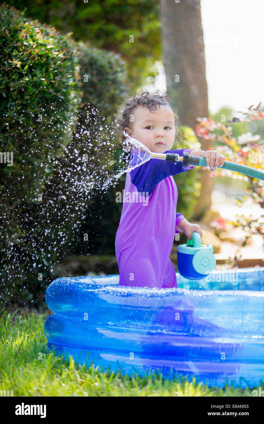 Candid portrait of a baby girl with hosepipe in paddling pool Stock Photo