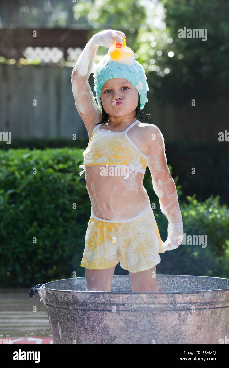 Portrait of girl standing in bubble bath in garden holding rubber duck on head Stock Photo