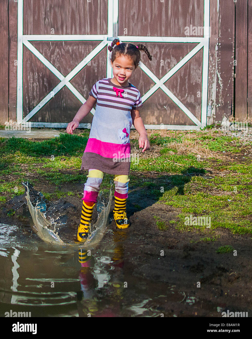 Girl stamping and splashing in garden puddle Stock Photo