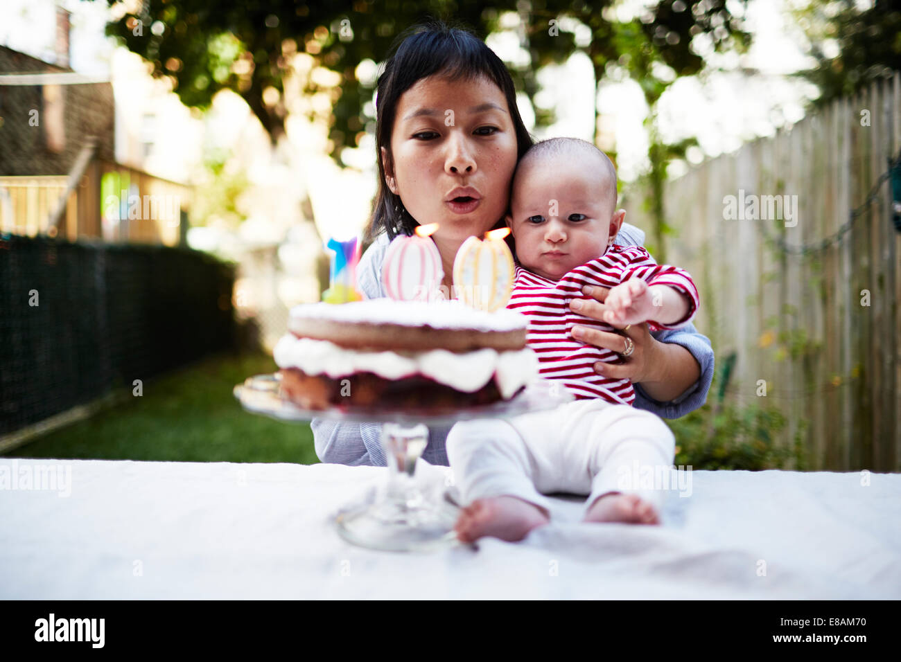 Mother holding baby son, blowing out candles on cake Stock Photo