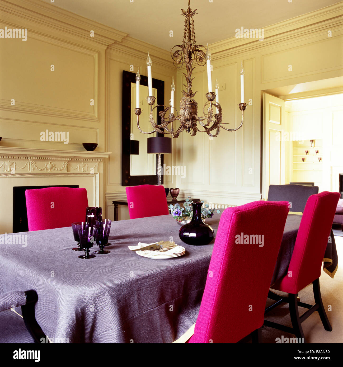 Ornate chandelier in dining room with bright pink upholstered chairs and pale mauve tablecloth Stock Photo