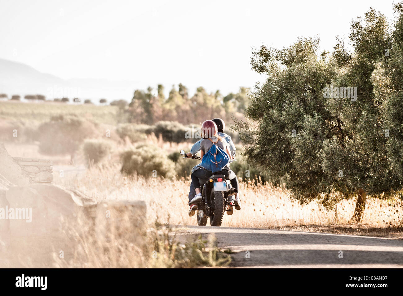 Rear view of mid adult couple riding motorcycle on dusty rural road, Cagliari, Sardinia, Italy Stock Photo