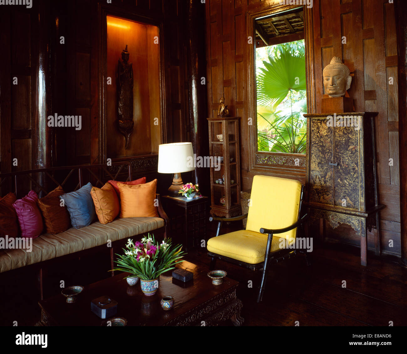 Brightly coloured cushions on sofa in panelled living room in Thailand Stock Photo