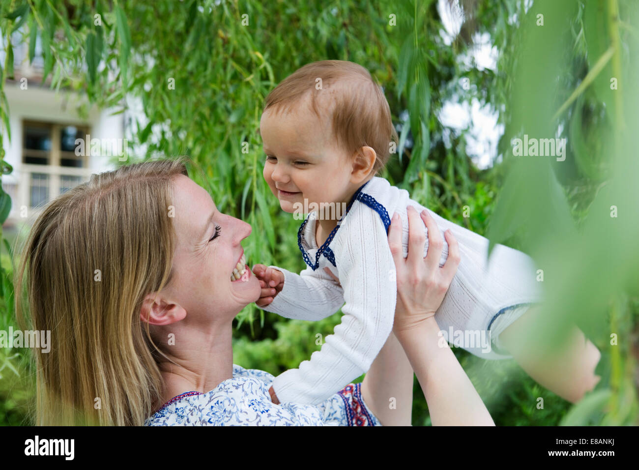Mother holding up baby daughter face to face in garden Stock Photo