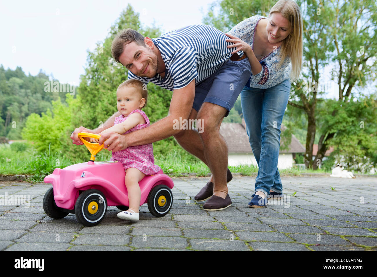 Mid adult couple pushing baby daughter on toy car in garden Stock Photo