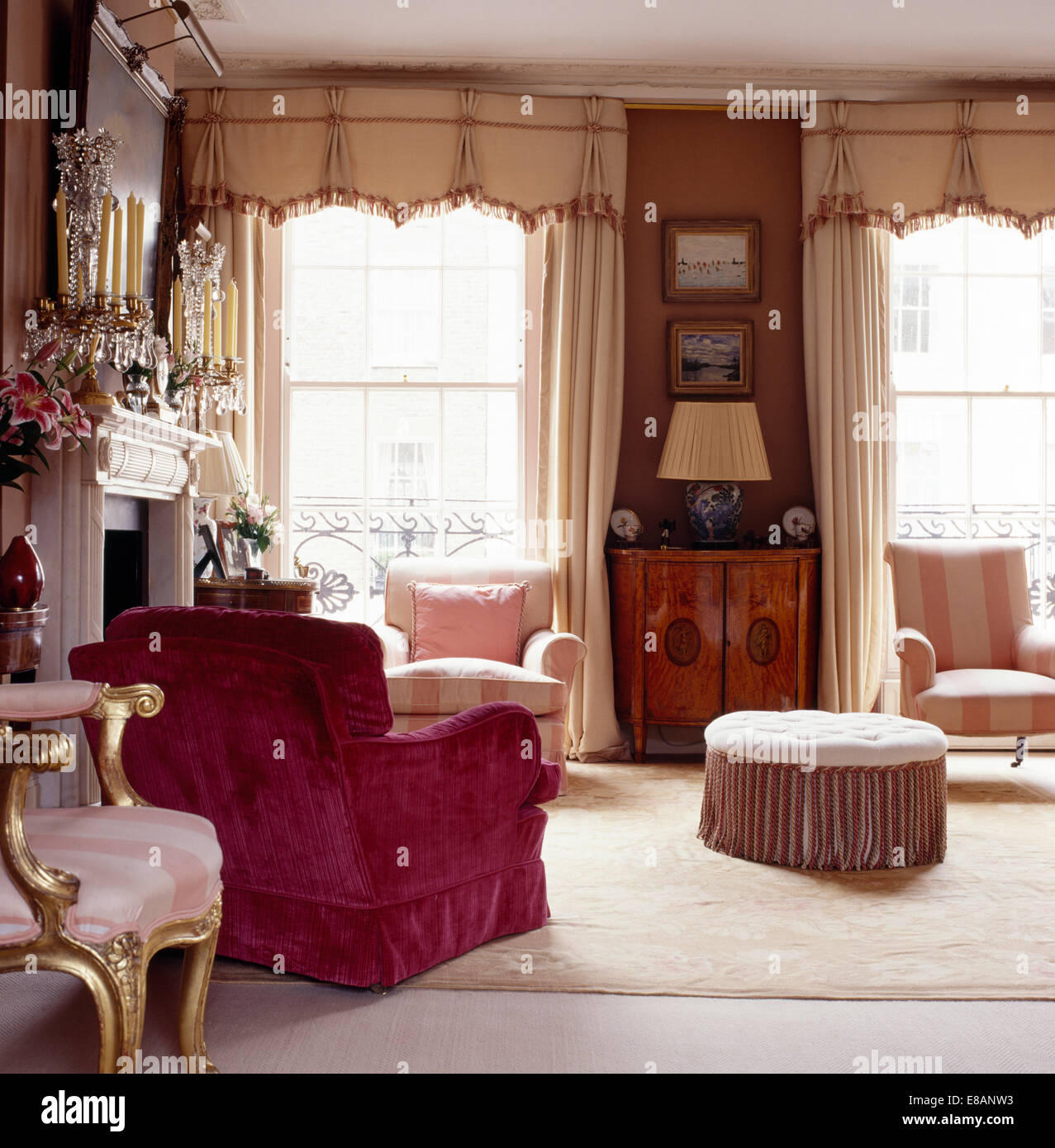 Pink velvet upholstered armchair in elegant townhouse living room with cream drapes and pelmets on windows Stock Photo