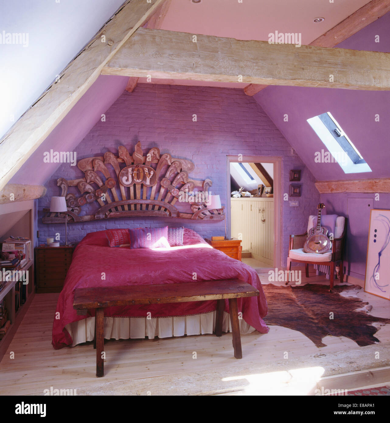 Large wooden carving above bed with pink bedcover in mauve attic bedroom Stock Photo