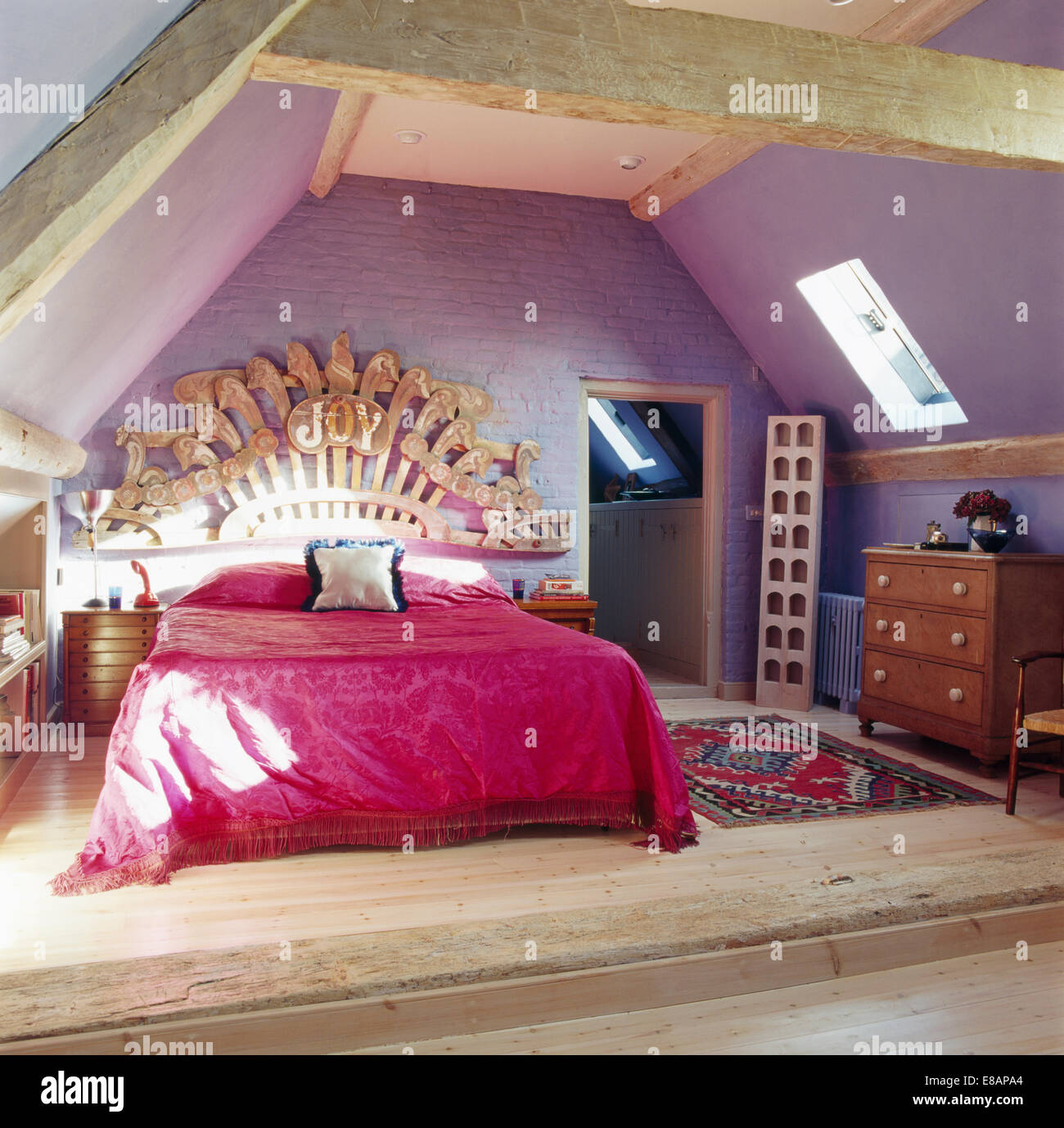 Large wooden carving above bed with pink bedcover in mauve attic bedroom Stock Photo