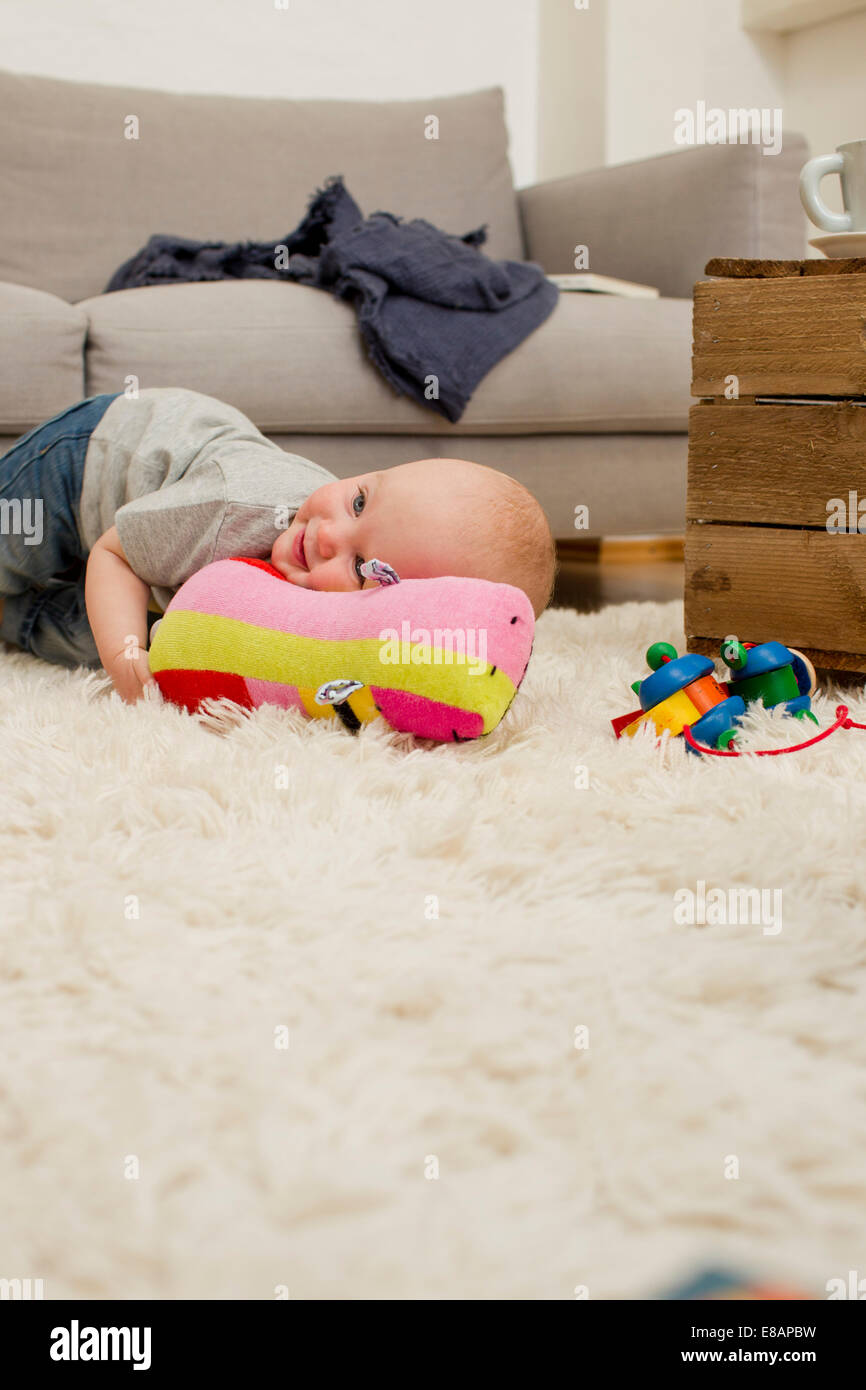 Baby girl lying on rug with soft toy in sitting room Stock Photo - Alamy