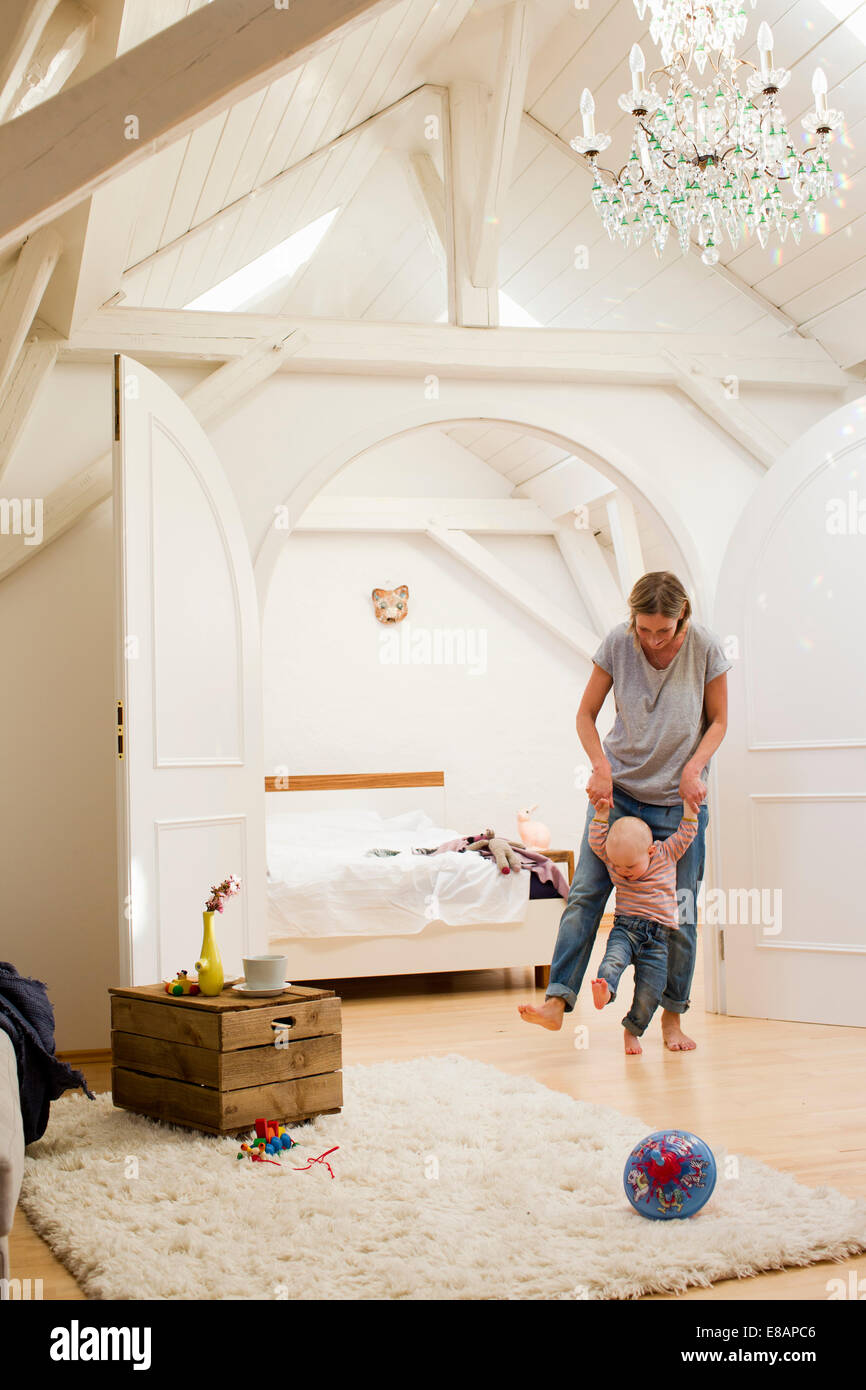 Mature mother and baby daughter walking together in sitting room Stock Photo