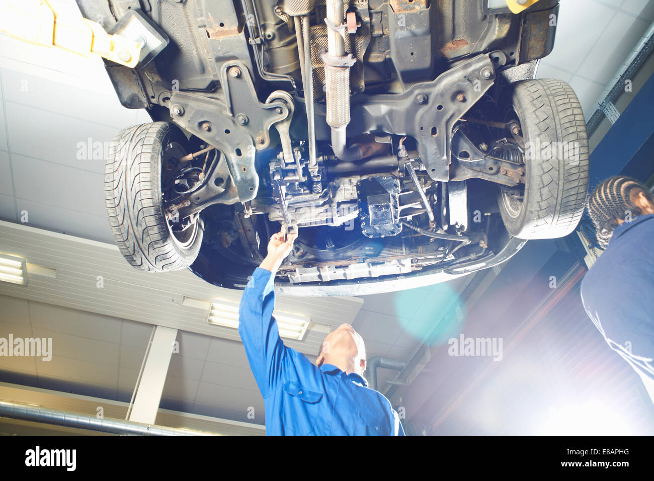 Male college student looking up at car in garage workshop Stock Photo