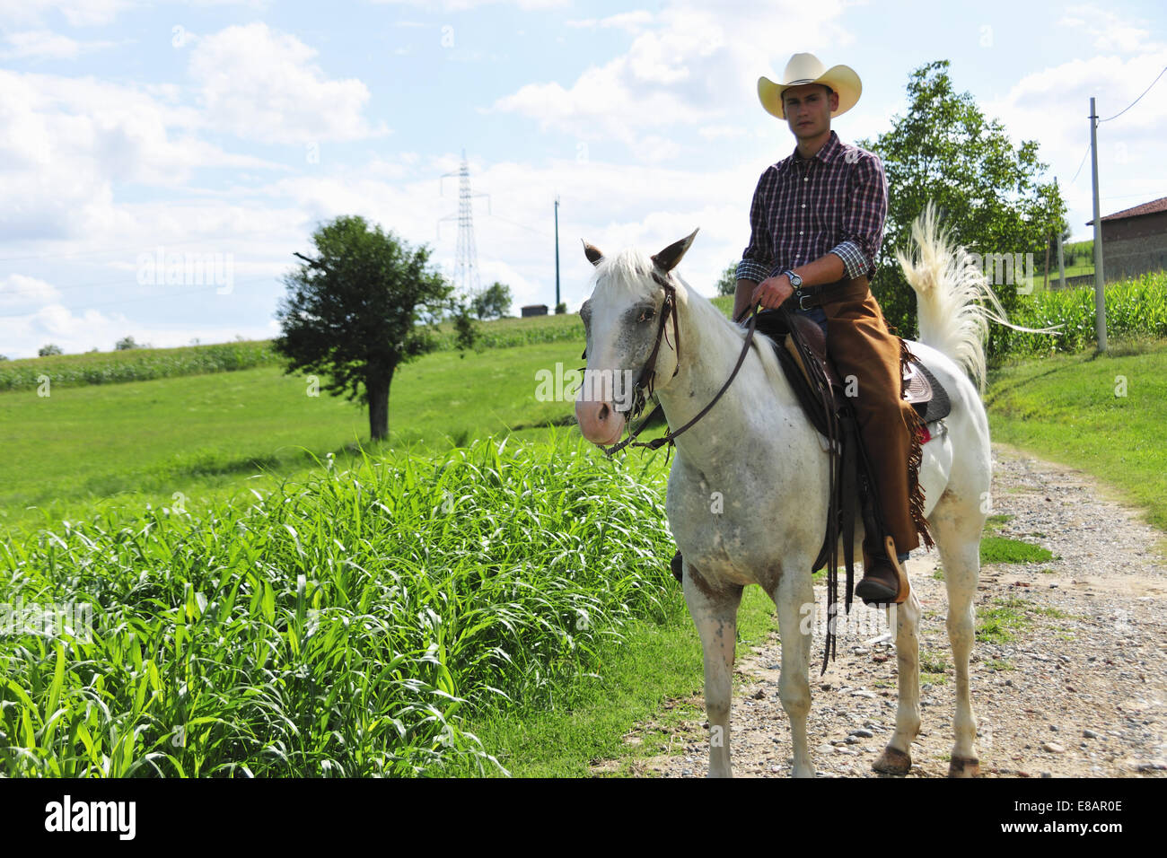 Portrait of young man in cowboy gear riding horse on rural road Stock Photo
