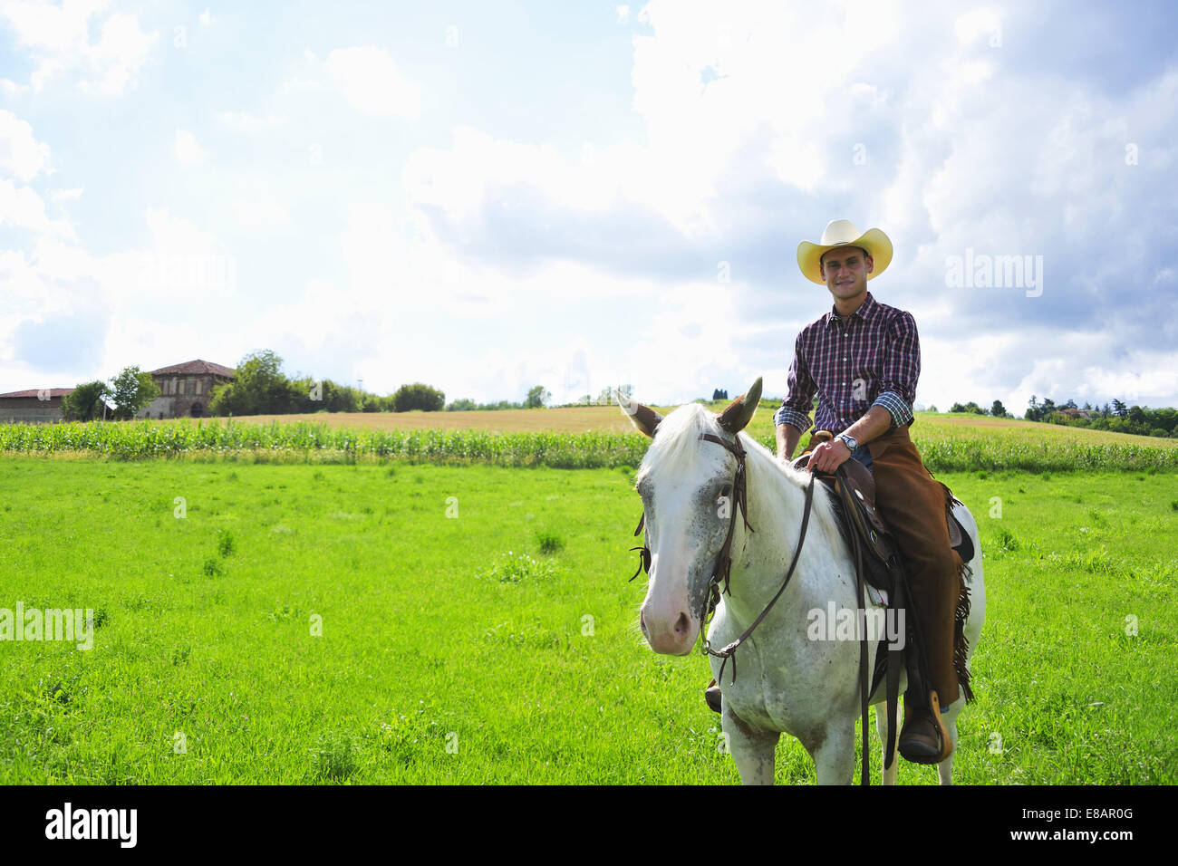 Portrait of young man in cowboy gear on horseback in field Stock Photo