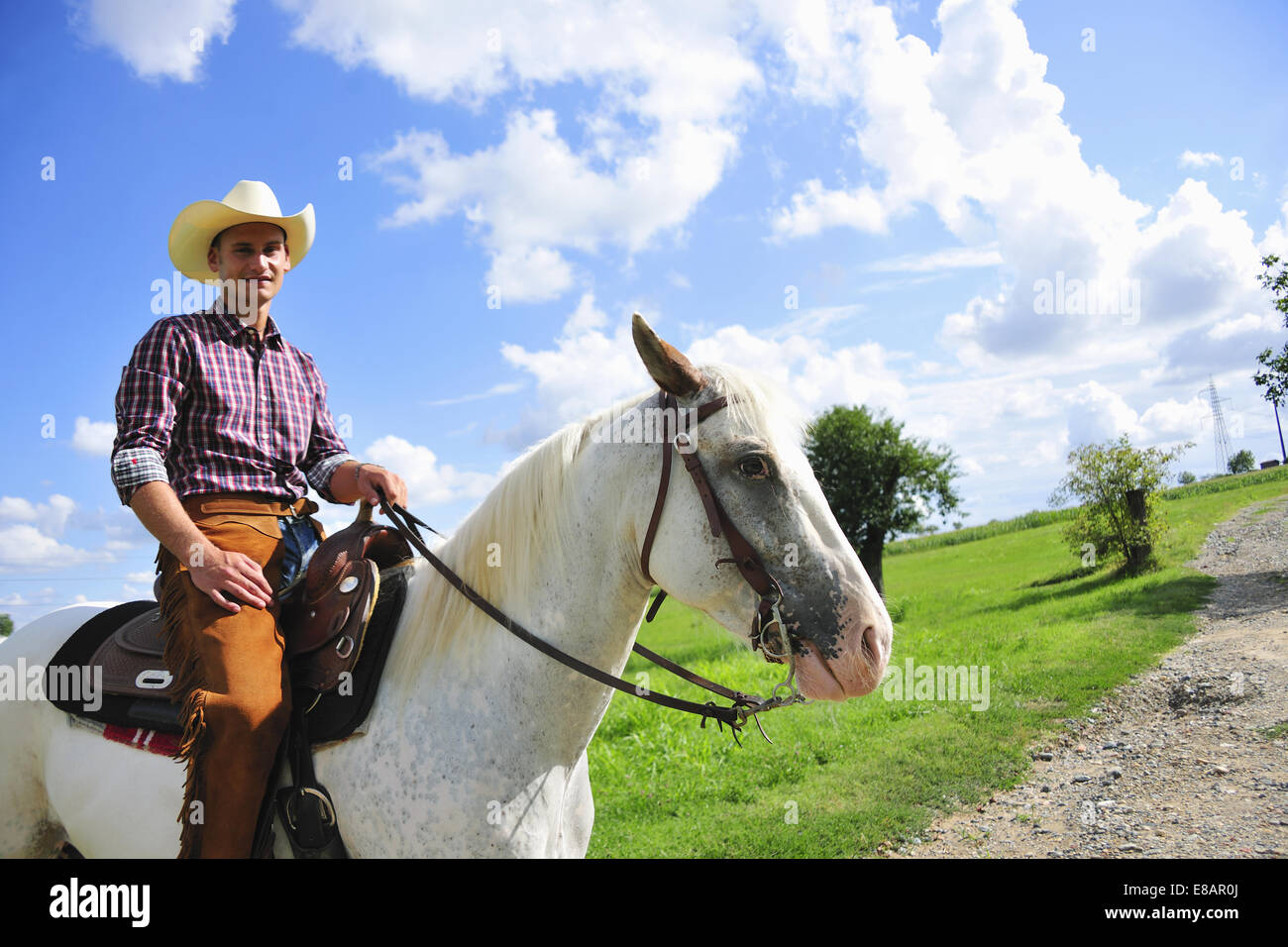 Portrait of young man in cowboy gear on horse on rural road Stock Photo